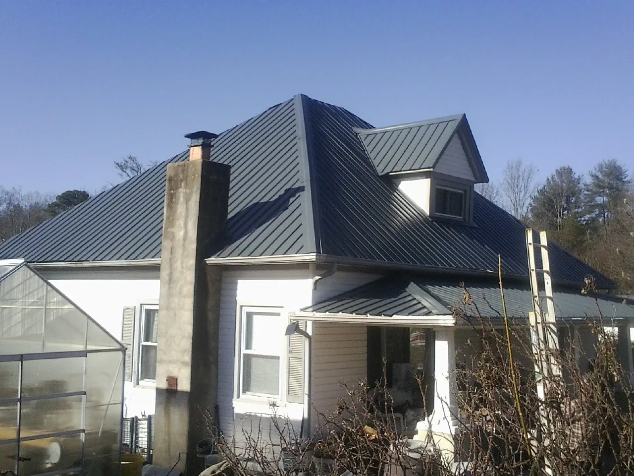 Dark blue standing seam metal roof on a white farmhouse with dormer — Slate & Tile Roof Repair by Roofing Brothers in Coal Creek