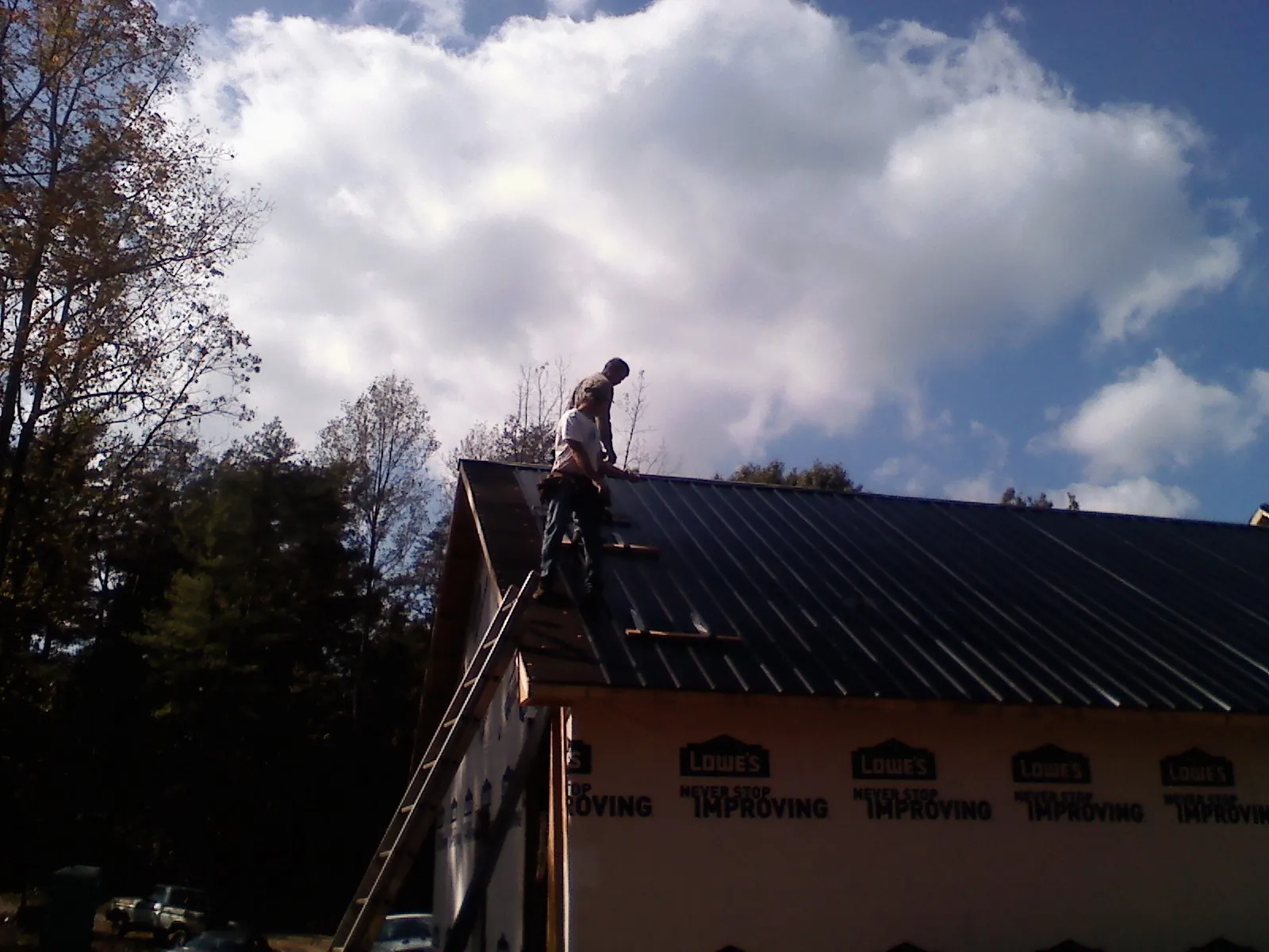 Roofer fastening dark metal panels high against a cloudy sky, from a Roof Inspection job in Coal Creek