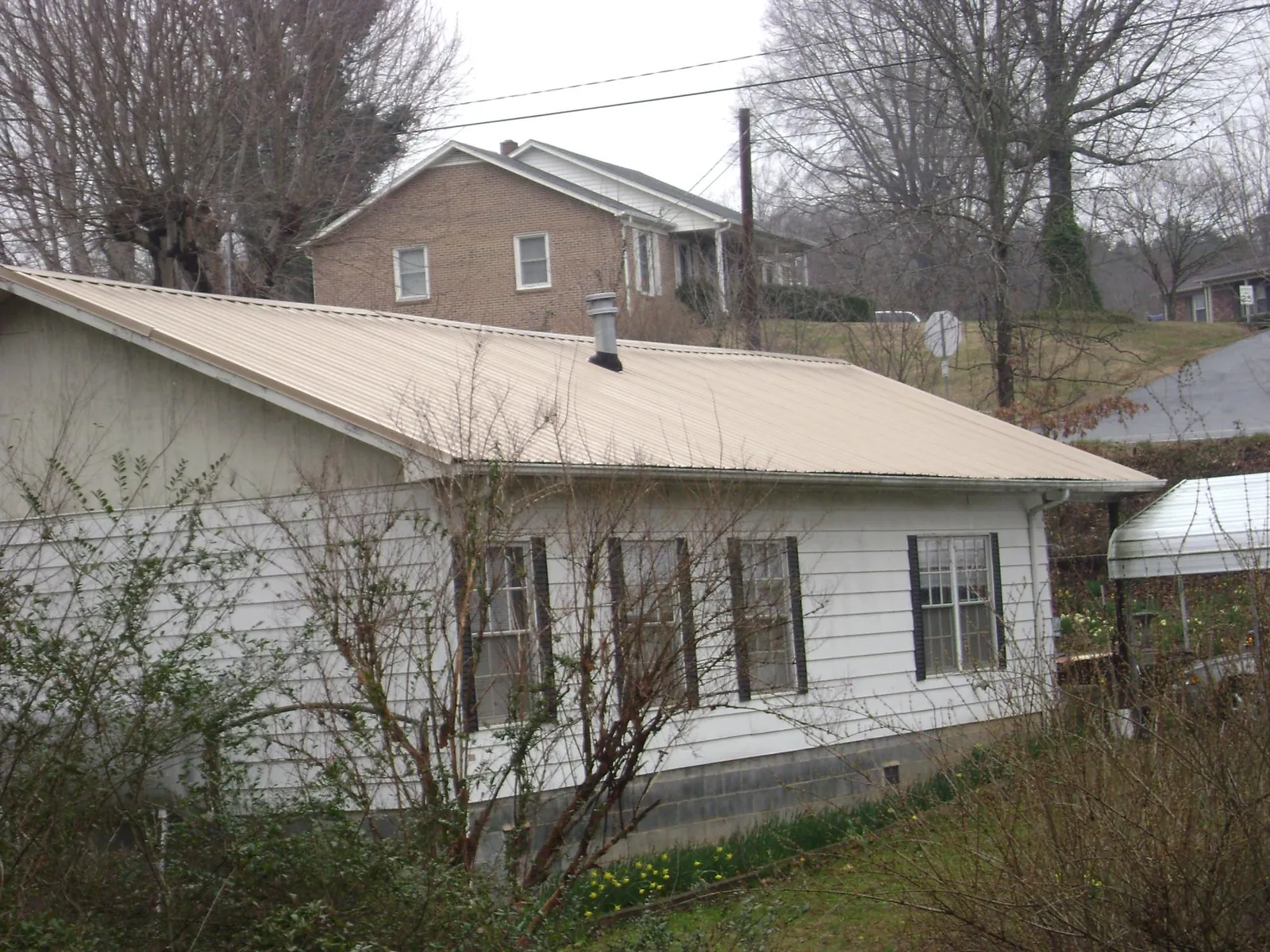 Tan metal roof on a white sided house set into a hillside — Commercial Roofing by Roofing Brothers in Coal Creek
